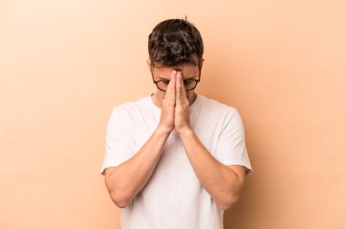 Beyaz tenli genç adam bej arka planda izole edilmiş dua ediyor, bağlılık gösteriyor, dindar biri ilahi ilham arıyor..