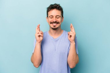 Kafkasyalı genç adam mavi arka planda izole edilmiş şans dilemek için şans diliyor.