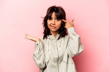 Pembe arka planda izole edilmiş genç İspanyol kadın elinde bir ürün tutuyor..