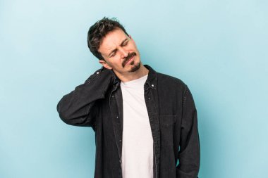 Kafkasyalı genç adam mavi arka planda izole edilmiş. Stres yüzünden boynu ağrıyor. Masaj yapıyor ve elle dokunuyor..