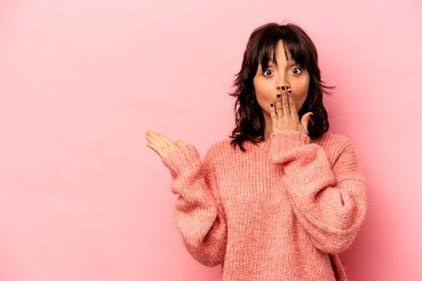 Pembe arka planda izole edilmiş genç İspanyol kadın avuç içi fotokopi alanını tutmaktan etkilenmiş..