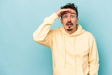 Mavi arka planda izole edilmiş genç beyaz adam yüksek sesle bağırıyor, gözleri açık ve elleri gergin tutuyor..