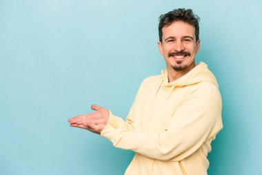 Mavi arka planda izole edilmiş genç beyaz bir adam palmiyesinde bir kopya alanı tutuyor..