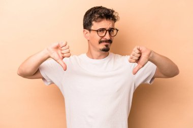 Beyazlı genç adam bej arka planda izole edilmiş baş parmağını aşağı gösteren, hayal kırıklığı konsepti.