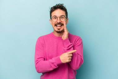 Kafkasyalı genç adam mavi arka planda izole edilmiş. Dedikodu yapıyor, bir şeyleri bildiriyor..