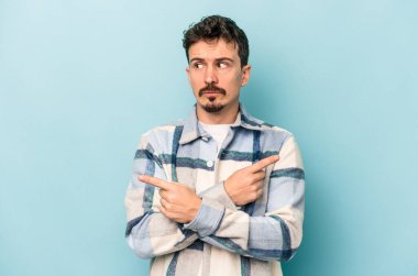 Mavi arka plan noktalarında izole genç beyaz adam, iki seçenek arasında seçim yapmaya çalışıyor.