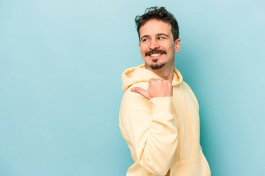 Kafkasyalı genç adam mavi arka plan noktalarında izole edilmiş başparmak uzakta, gülüyor ve kaygısız.