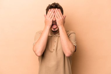 Beyaz tenli genç adam bej arka planda izole edilmiş. Yüzünün yarısını palmiye ile örterek eğleniyor..