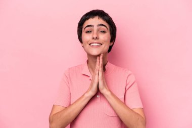 Pembe arka planda soyutlanmış genç beyaz bir kadın el ele tutuşup ağzının kenarında dua ediyor, kendinden emin hissediyor..