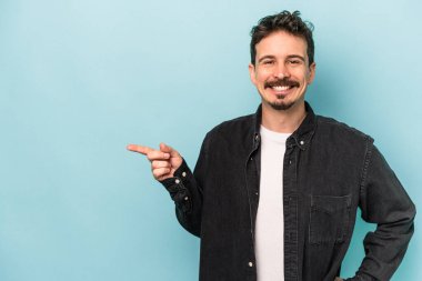 Mavi arka planda izole edilmiş genç beyaz adam işaret parmağıyla işaret ederek gülümsüyor..