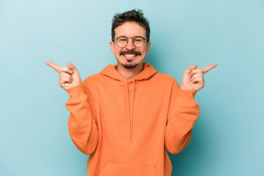 Mavi arka planda izole edilmiş genç beyaz adam farklı kopya alanlarını gösteriyor, birini seçiyor, parmaklarıyla gösteriyor.