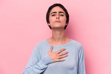 Pembe arka planda izole edilmiş genç beyaz kadın yemin ediyor, elini göğsüne koyuyor..