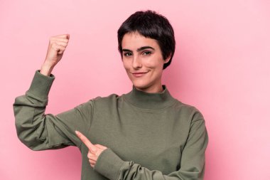 Pembe arka planda izole edilmiş genç beyaz kadın güçlü bir hareket gösteriyor. Kollarıyla, kadınsı gücün sembolü.