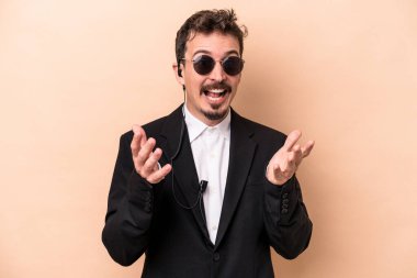 Beyaz tenli genç koruma bej arka planda izole edilmiş. Hoş bir sürpriz bekliyor. Heyecanlı ve el kaldırıyor..