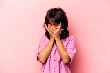 Pembe arka planda izole edilmiş genç İspanyol kadın kameraya parmaklarıyla göz kırpıyor, yüzünü kapatmaktan utanıyor..