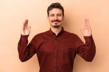 Beyaz tenli genç adam bej arka planda izole edilmiş. Elinde parmakları olan, gülümseyen ve kendinden emin bir şey var..