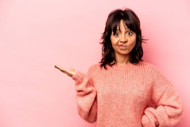 Pembe arka planda izole edilmiş genç İspanyol kadın avucunun içinde bir fotokopi alanı ve belinde bir el daha gösteriyor..