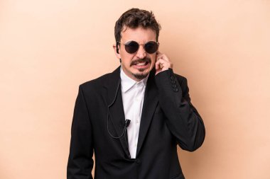 Beyaz tenli genç koruma bej arka planda izole edilmiş kulakları elleriyle kapatıyor..