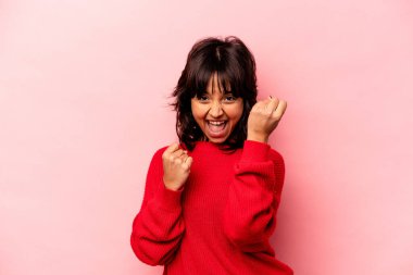 Genç İspanyol kadın pembe arka planda izole edilmiş kaygısız ve heyecanlı tezahüratlar yapıyor. Zafer konsepti.