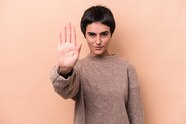 Young caucasian woman isolated on beige background standing with outstretched hand showing stop sign, preventing you.