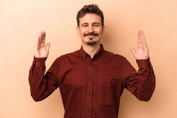 stock image Young caucasian man isolated on beige background holding something little with forefingers, smiling and confident.