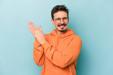 Kafkasyalı genç adam mavi arka planda izole edilmiş enerjik ve rahat hissediyor, ellerini ovuşturuyor kendinden emin.