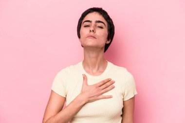 Pembe arka planda izole edilmiş genç beyaz kadın yemin ediyor, elini göğsüne koyuyor..