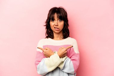 Genç İspanyol kadın pembe arka planda iki seçenek arasında seçim yapmaya çalışıyor..