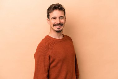 Beyaz tenli genç adam bej arka planda izole edilmiş. Kendine güveniyor. Kalçaları tutuyor..