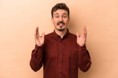 Beyaz tenli genç adam bej arka planda izole edilmiş. Kahkahalar atıyor..