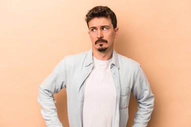 Kafkasyalı genç adam bej arka planda izole, kafası karışmış, şüpheli ve güvensiz hissediyor..