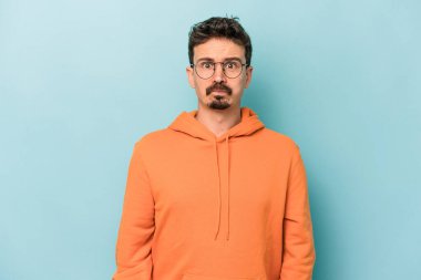 Mavi arka planda izole edilmiş genç beyaz adamın yanakları şişer, yorgun bir ifadesi vardır. Yüz ifadesi kavramı.