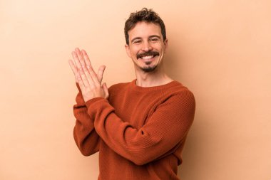 Beyaz tenli genç adam bej arka planda izole edilmiş enerjik ve rahat hissediyor, ellerini ovuşturuyor kendinden emin..