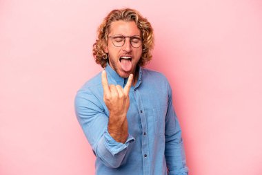 Pembe arka planda izole edilmiş genç beyaz adam parmaklarıyla taş hareketi gösteriyor.