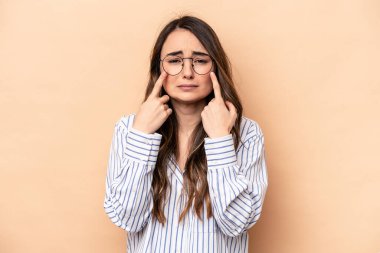 Beyaz tenli genç bir kadın bej arka planda izole edilmiş ağlıyordu, bir şeyden mutsuzdu, acı ve kafa karışıklığı içeriyordu..