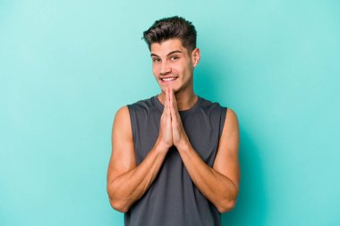 Mavi arka planda izole edilmiş genç beyaz bir adam el ele tutuşup, ağzının kenarında dua ediyor, kendinden emin..