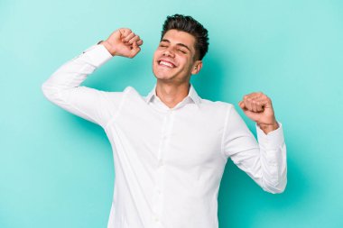 Mavi arka planda izole edilmiş genç beyaz adam kollarını uzatıyor, rahat bir konumda..