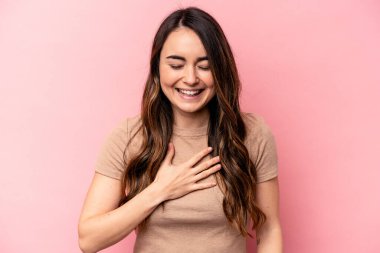 Pembe arka planda soyutlanmış beyaz bir kadın yüksek sesle gülüyor ve elini göğsüne koyuyor..