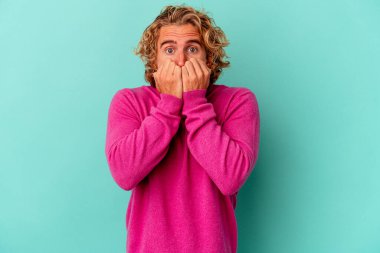 Mavi arka planda izole edilmiş, tırnak yiyen, gergin ve endişeli genç bir beyaz adam..