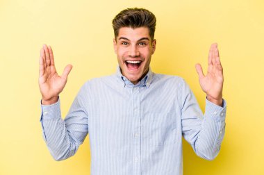Sarı arka planda izole genç beyaz adam hoş bir sürpriz alıyor, heyecanlı ve el kaldırıyor..