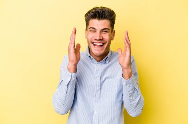 Sarı arka planda izole edilmiş genç beyaz adam yüksek sesle gülüyor ve elini göğsüne koyuyor..