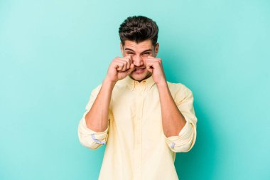 Kafkasyalı genç adam mavi arka planda izole edilmiş sızlanıyor ve ağlıyordu..