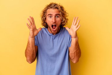 Sarı arka planda izole edilmiş genç beyaz bir adam zaferi ya da başarıyı kutluyor, şaşırıyor ve şok oluyor..