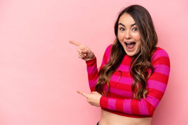 Pembe arka planda izole edilmiş genç beyaz kadın işaret parmaklarıyla işaret ederek heyecanlanıyor..