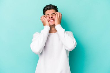 Kafkasyalı genç adam mavi arka planda izole edilmiş, ağlıyor, bir şeyden memnun değil, acı ve kafa karışıklığı konsepti..