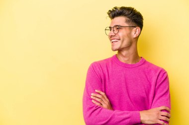 Sarı arka planda izole edilmiş genç beyaz adam kollarını kavuşturarak gülümsüyor..