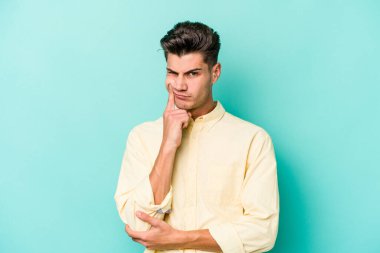 Mavi arka planda izole edilmiş genç beyaz adam alaycı bir ifadeyle kameraya bakarken mutsuz oluyor..