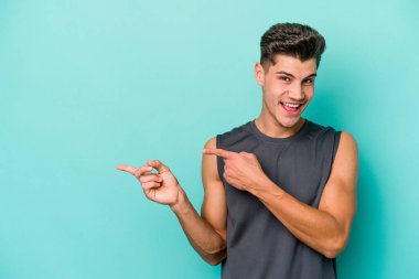 Mavi arka planda izole edilmiş genç beyaz adam işaret parmağıyla fotokopi alanını işaret ederek heyecan ve arzusunu ifade ediyor..