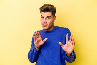 Sarı arka planda izole edilmiş genç beyaz adam tiksinti belirtisi gösteren birini reddediyor..