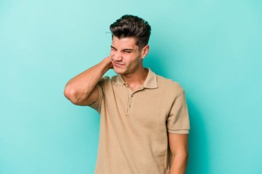 Kafkasyalı genç adam mavi arka planda izole edilmiş. Stres yüzünden boynu ağrıyor. Masaj yapıyor ve elle dokunuyor..